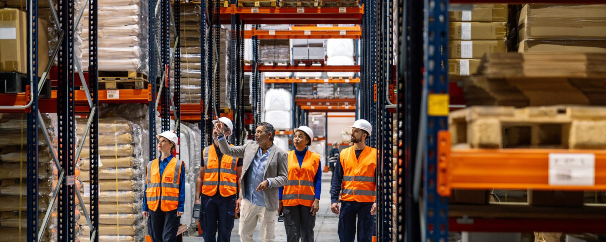 Diverse group of logistics workers and a manager inspecting inventory and discussing operations in a large distribution warehouse